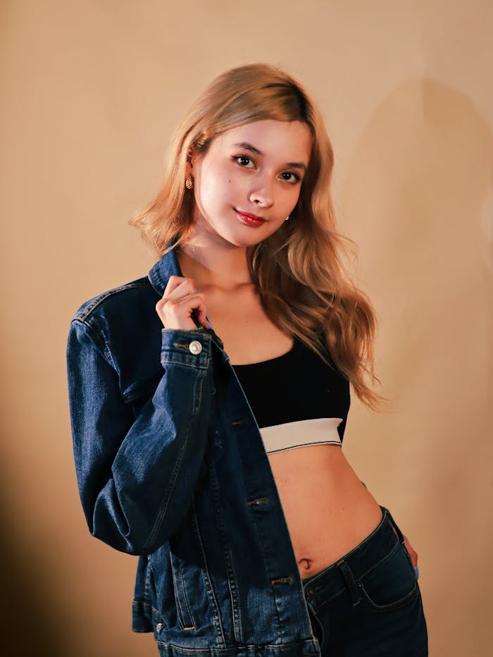 Fashionable young woman in denim jacket posing confidently indoors with warm lighting.